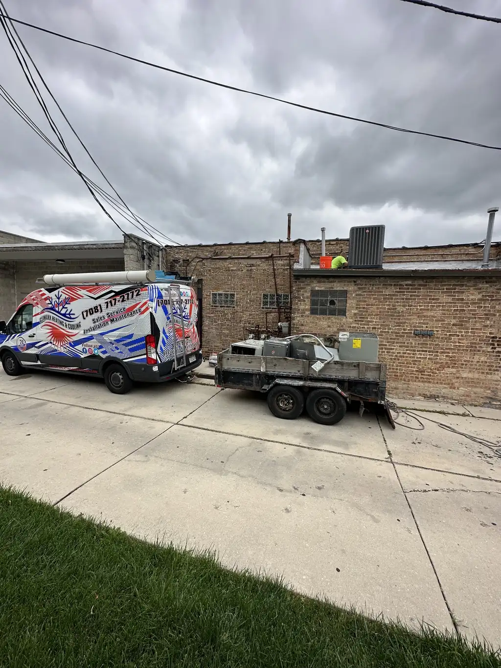 The Climaxx van and equipment trailer parked behind a brick building on a job